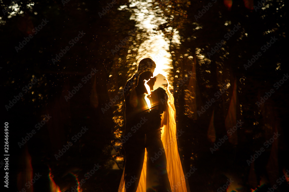 Evening summer sun makes a halo around beautiful wedding couple hugging in the park