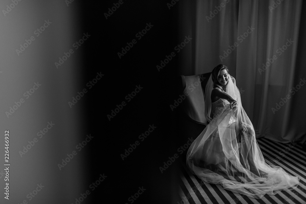 Look from behind the door at charming bride sitting in a big chair in hotel room Look from behind the door at charming bride sitting in a big chair in hotel room