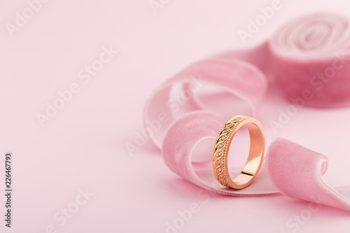 Pink gold wedding ring with diamonds and wave pattern on pink background
