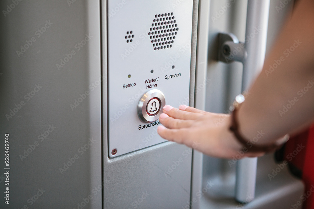 The person presses the button to call and talk with the support service of the train or subway. The inscription in German is translated as Call station - Operation - Service - Listen - Speak. The person presses the button to call and talk with the support service of the train or subway. The inscription in German is translated as Call station - Operation - Service - Listen - Speak.