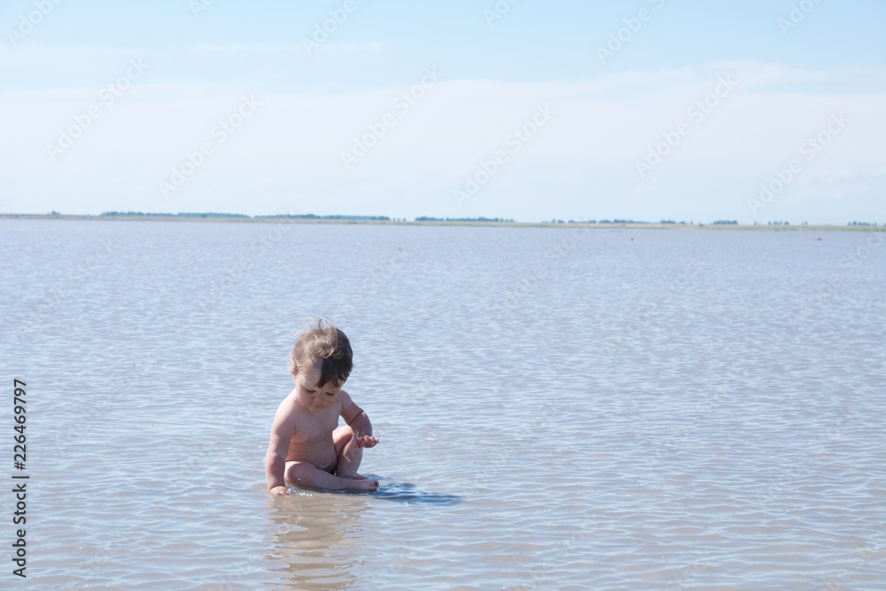 Sitting baby among the lake at summer. Salt shallow lake in Russia. Loneliness  concept in big world