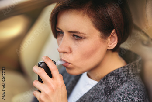 Young millennial woman using breath alcohol analyzer in the car. Closeup with selective focus. Girl taking alcohol test with breathalyzer. photo