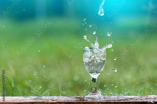 Drink water pouring in to glass over sunlight and natural green background.Select focus blurred background.Fresh Clean water splash.
