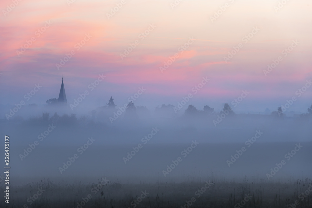 Church tower and village in fog at dawn