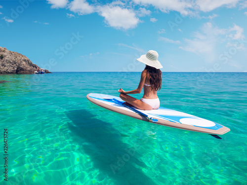 A beautiful young woman relaxes on a SUP board in the sea near the island. Standup paddleboarding on Hawaii.