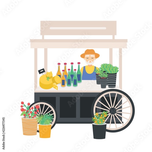 Seller standing at wheeled cart, counter, stall or kiosk with cheese, wine bo...