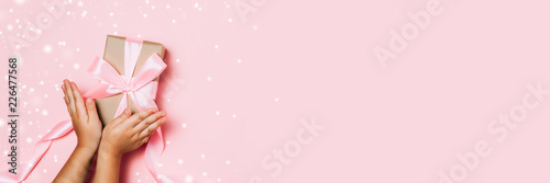 Child hands holding beautiful gift box on pink background © paninastock