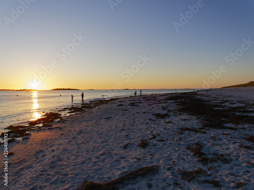 People standing at the waters edge on Plage Sainte-Marguerite in Brittany watching the setting sun. photo