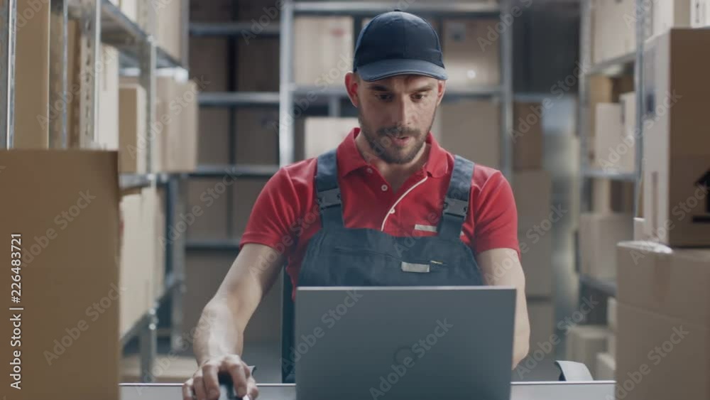 Uniformed Worker Uses Laptop while Sitting at His Desk in the Warehouse. Uniformed Worker Uses Laptop while Sitting at His Desk in the Warehouse.