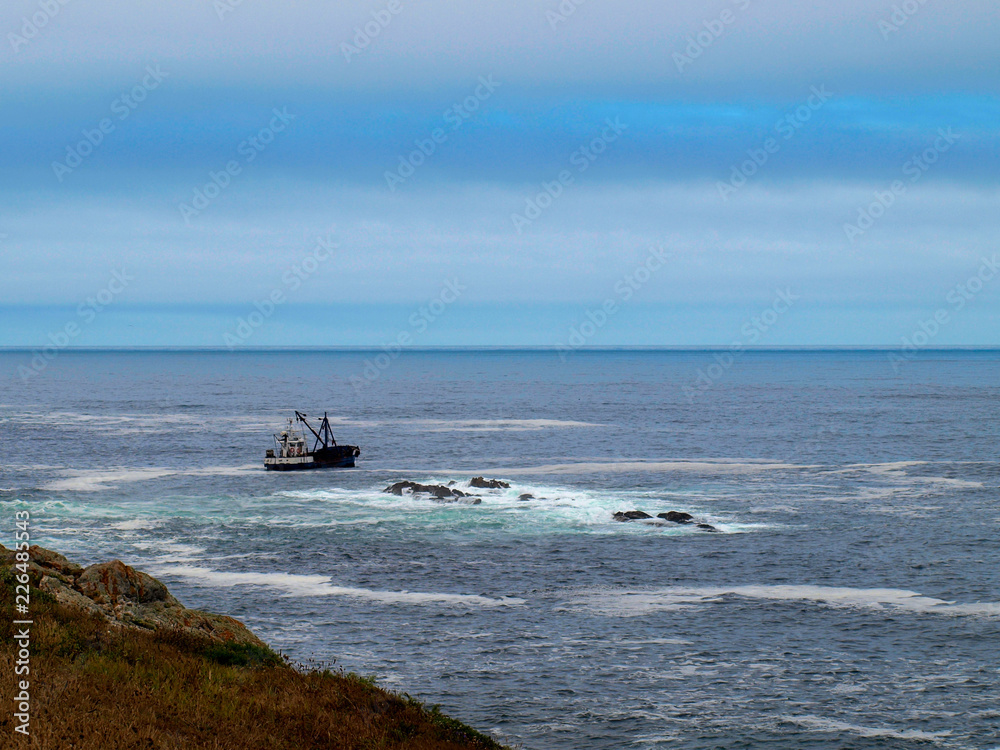 Obraz premium Fishing boat near rocks at the sea