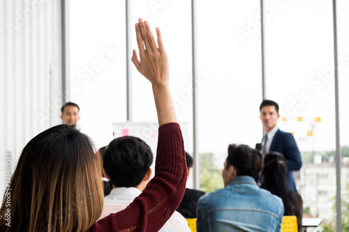 A woman is raising hand up while businessman is speaking in training at the office.