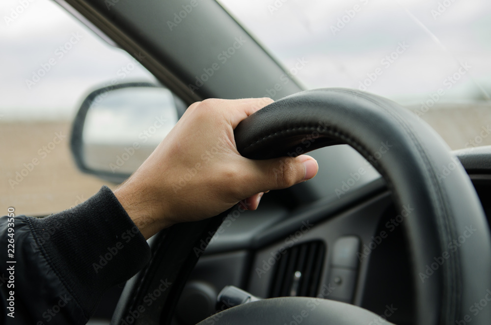 man's hand on the black leather steering wheel in the car