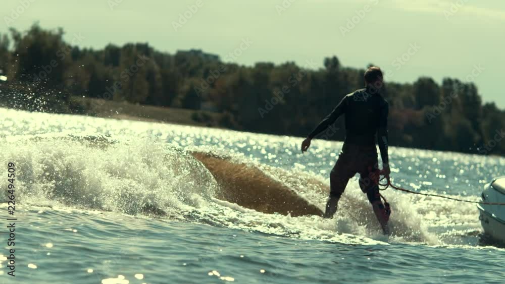 Extreme water sports. Man riding board on waves of river. Wake surfing rider training on surf board in slow motion. Young sportive man water skiing. Extreme lifestyle Extreme water sports. Man riding board on waves of river. Wake surfing rider training on surf board in slow motion. Young sportive man water skiing. Extreme lifestyle