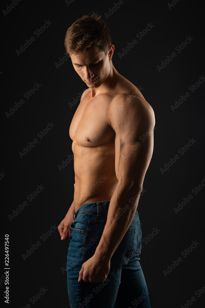 Fototapeta premium young, Strong bodybuilder with six packs. Bodybuilder flexes muscles against dark background