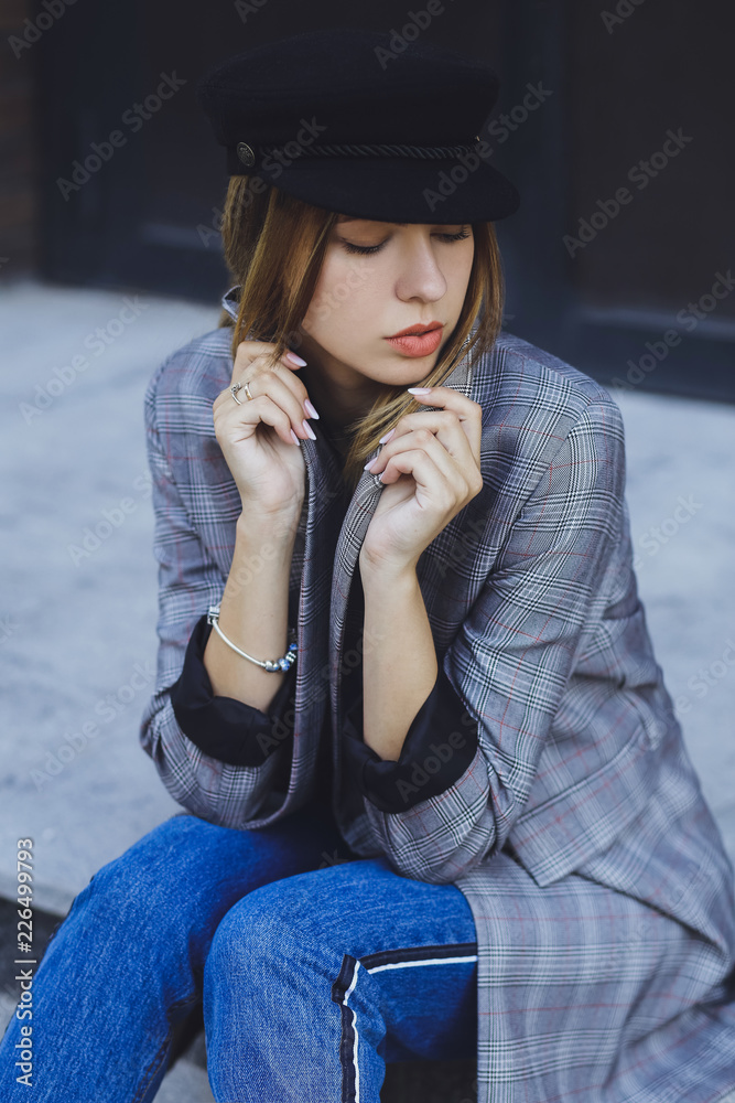 Young beautiful girl in a jacket, jeans and hat on a brick wall background