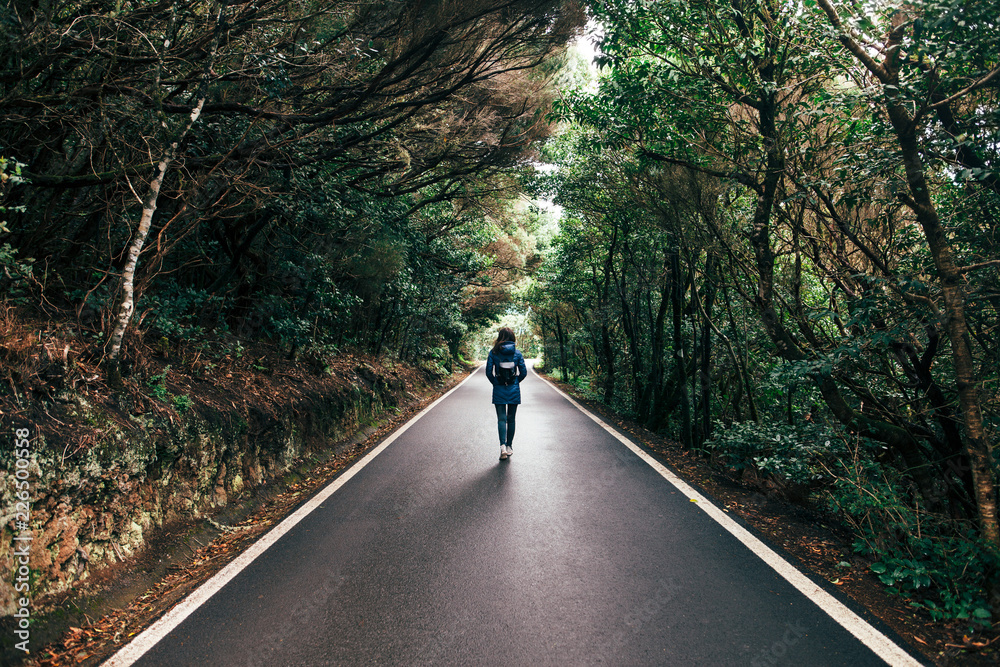 Young traveler woman walking on the road and forest background