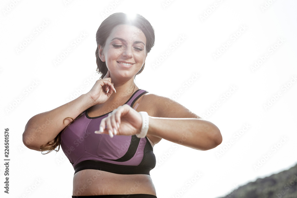 Pulse measurement. Joyful nice woman looking at her watch while measuring her heart rate Pulse measurement. Joyful nice woman looking at her watch while measuring her heart rate