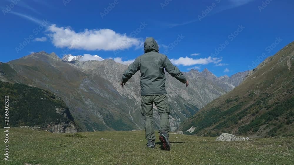 Slow motion - hiker man standing on the edge of the cliff and raising her hands up against high rocky mountains sunbathing in morning sun. Happy man enjoying success and stunning view. Slow motion - hiker man standing on the edge of the cliff and raising her hands up against high rocky mountains sunbathing in morning sun. Happy man enjoying success and stunning view.
