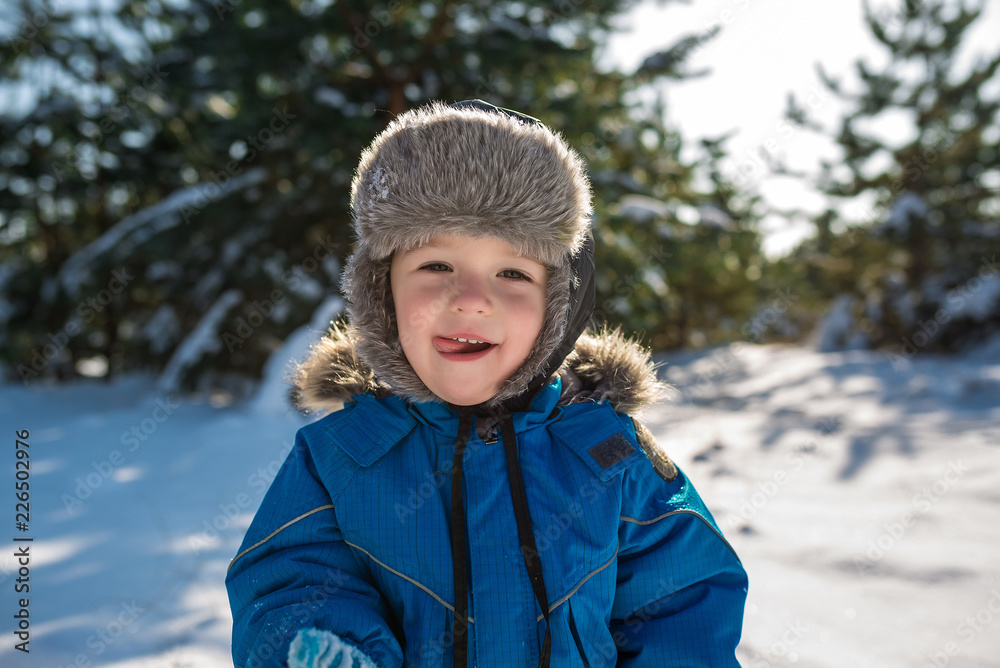 Happy cute little boy dressed in warm coverall and hat in winter frozen snowy forest Happy cute little boy dressed in warm coverall and hat in winter frozen snowy forest