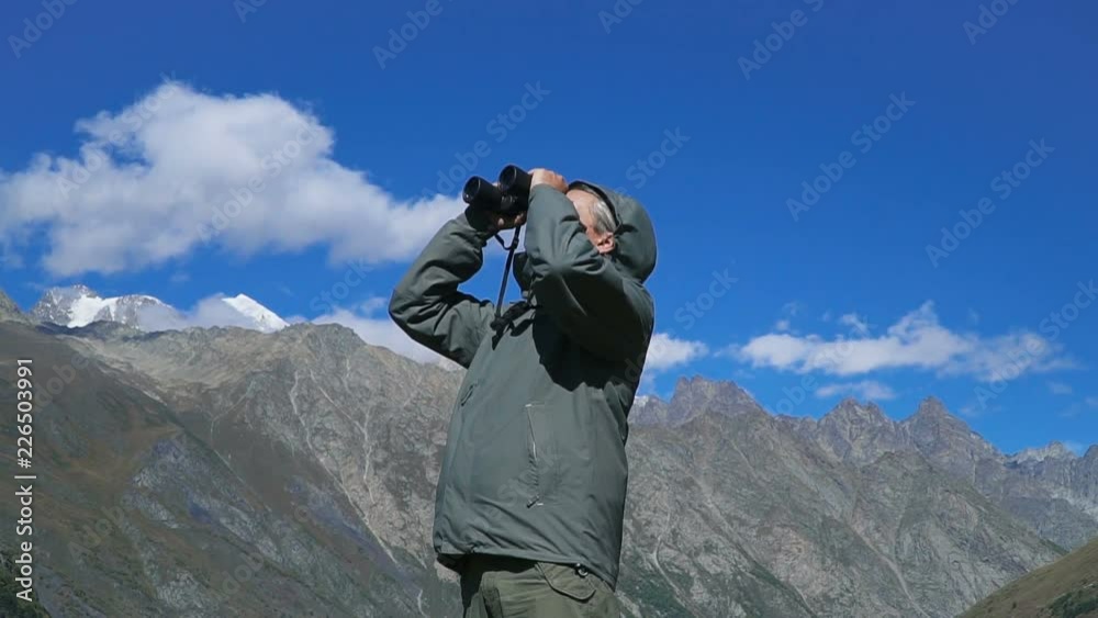 Man looking through binoculars at the mountains, enjoying the view at Caucasus mountains. Man looking through binoculars at the mountains, enjoying the view at Caucasus mountains.