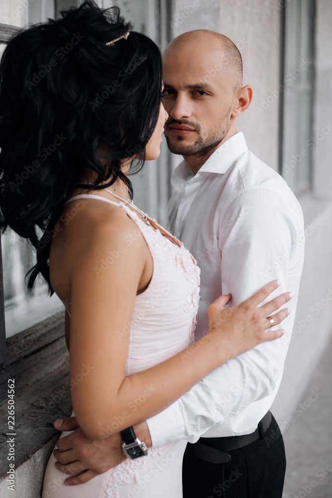 Naklejka premium Handsome young bald headed man hugs with passion young brunette in pink evening dress