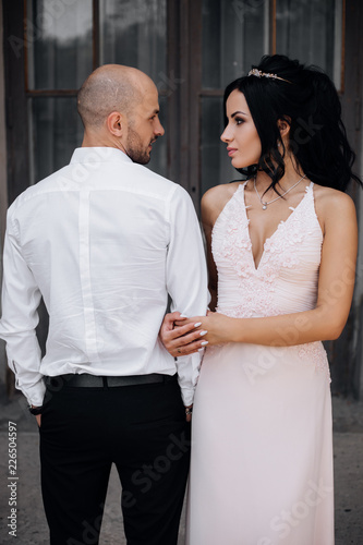 Handsome young bald headed man hugs with passion young brunette in pink evening dress