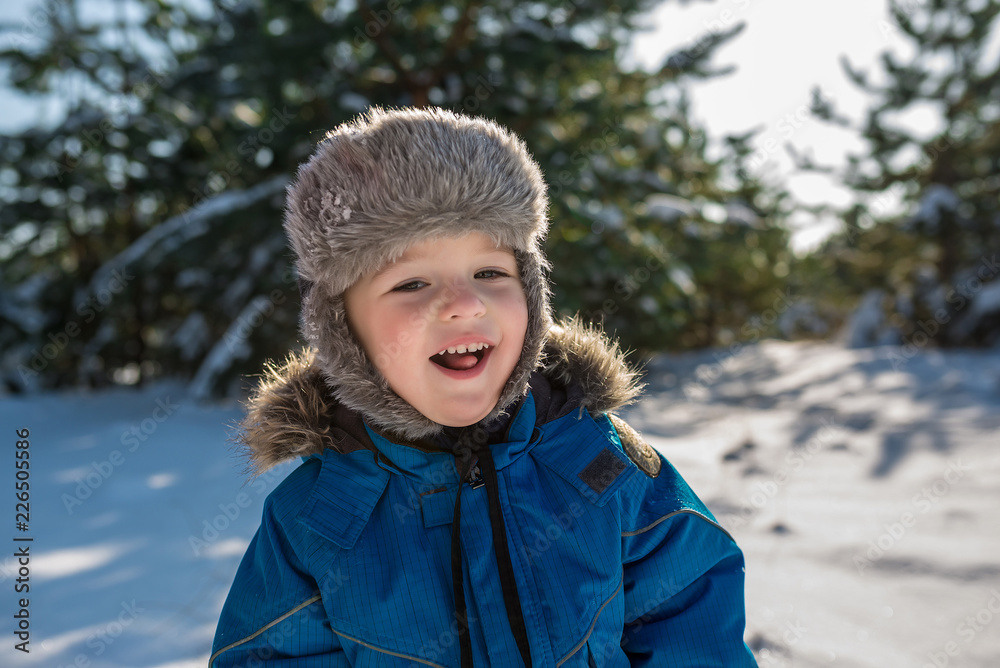 Happy cute little boy dressed in warm coverall and hat in winter frozen snowy forest