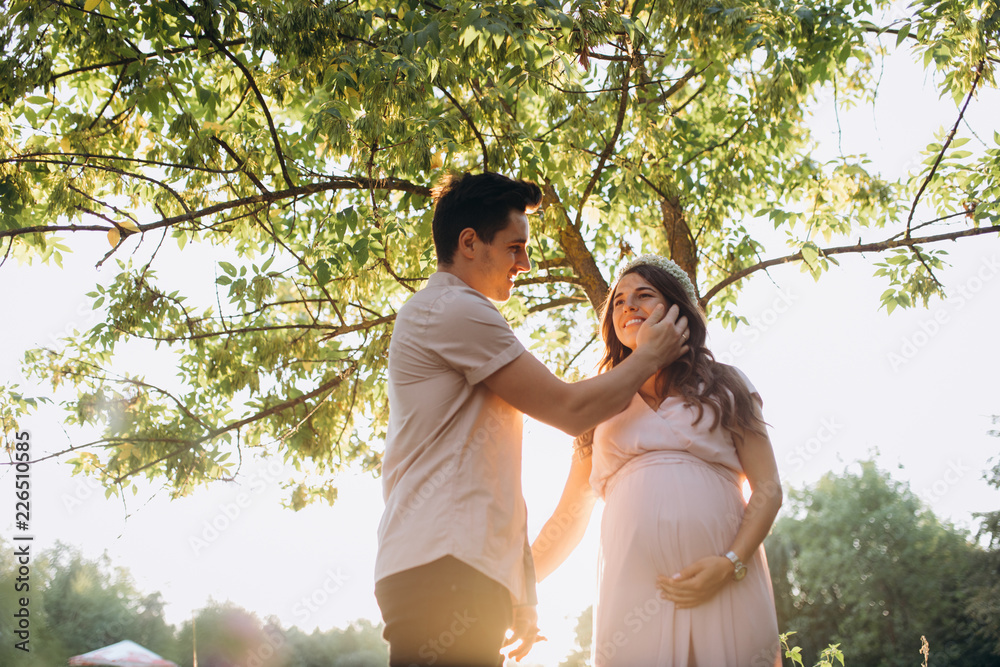 Man hugs beautiful pregnant woman tender standing before the lake in the rays of evening sun Man hugs beautiful pregnant woman tender standing before the lake in the rays of evening sun