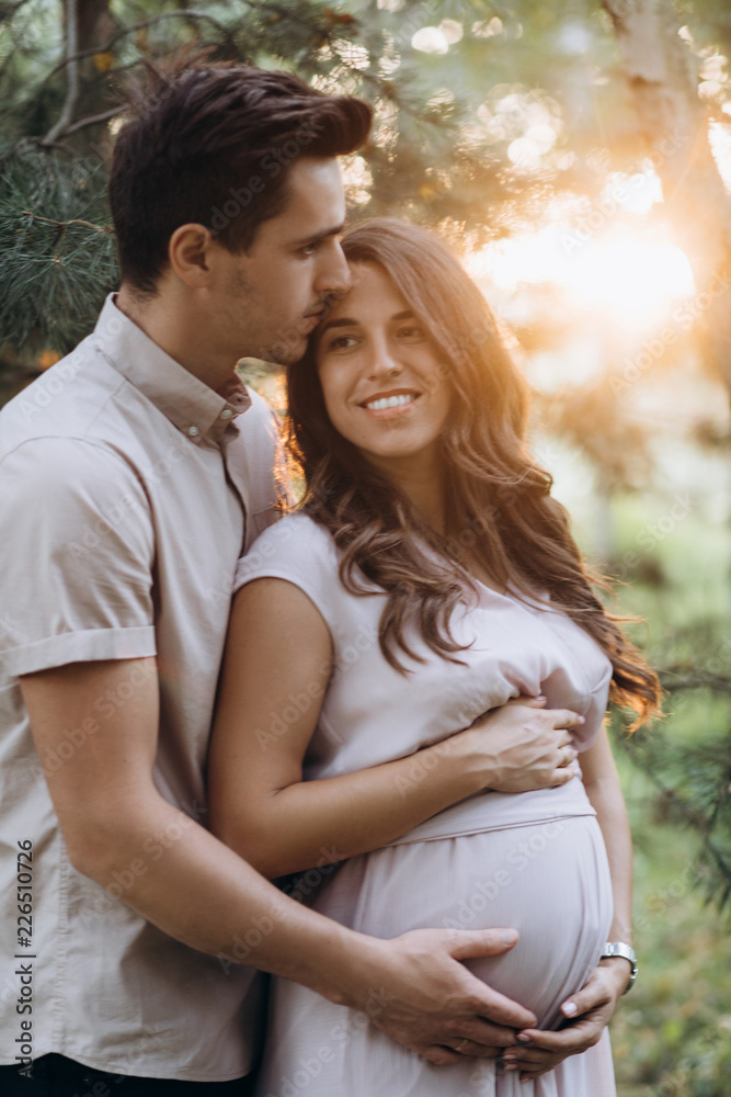 Man hugs beautiful pregnant woman tender standing before the lake in the rays of evening sun Man hugs beautiful pregnant woman tender standing before the lake in the rays of evening sun