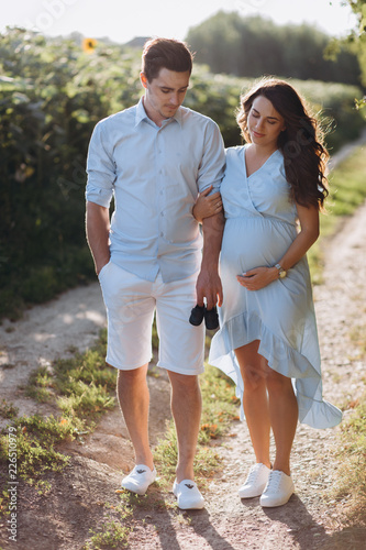 Expecting man and woman walk along the path across the field with sunflowers in beautiful summer evening