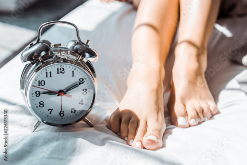 Canvas Print close-up partial view of female feet and alarm clock on bed