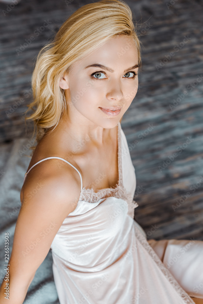 high angle view of beautiful blonde girl sitting and smiling at camera in bedroom high angle view of beautiful blonde girl sitting and smiling at camera in bedroom