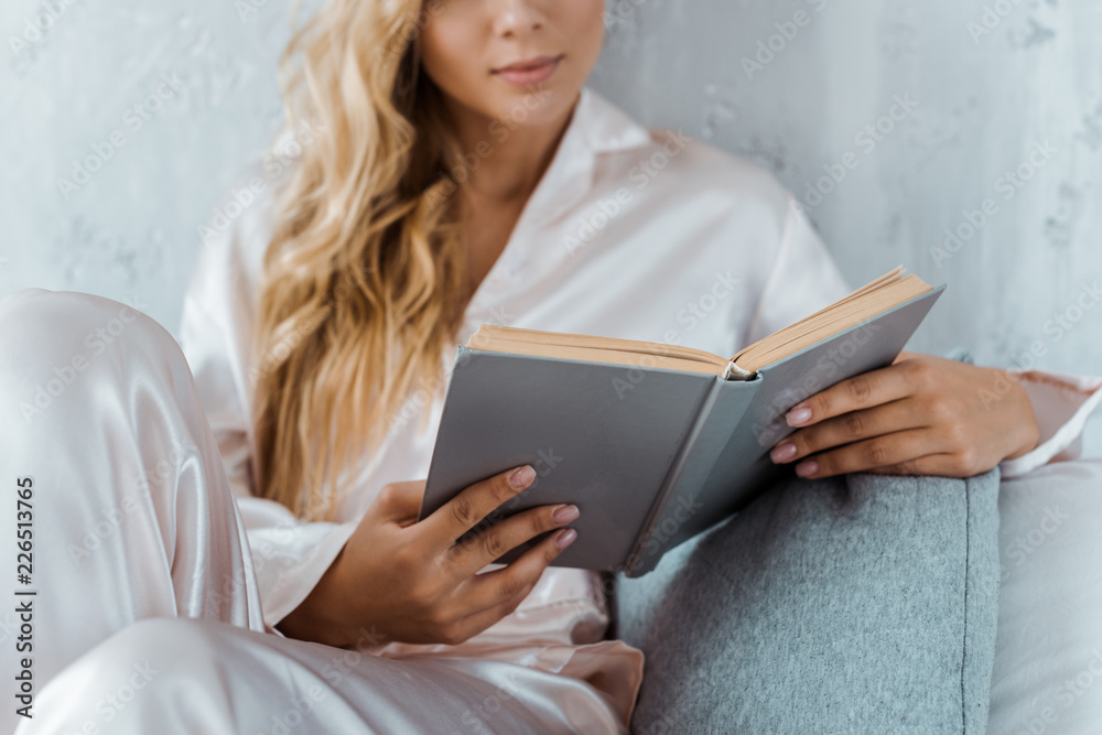 cropped shot of young woman in pajamas sitting on bed and reading book cropped shot of young woman in pajamas sitting on bed and reading book