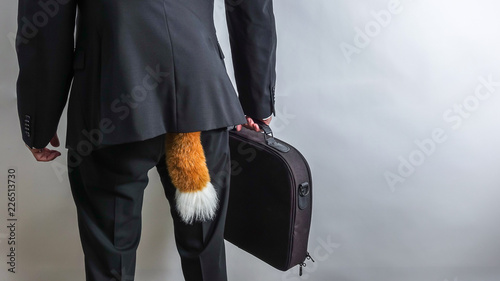 Sneaky businessman in black suit with a briefcase and a fox tail. Concept for economic / white collar crime, fraud and black market. White background with copy space for text.