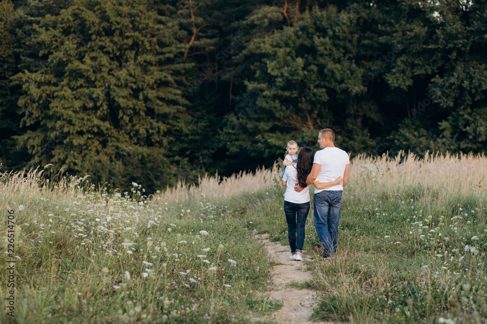 Warm hugs of young parents and their little daughter standing in the summer field