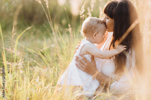 Beautiful portrait of charming mother and lovely little daughter walking across the field in the rays of evening sun