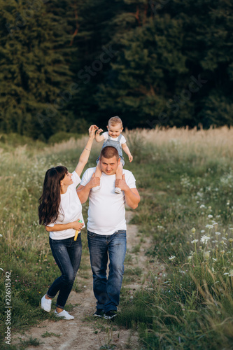 Warm hugs of young parents and their little daughter standing in the summer field
