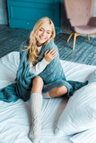 smiling attractive woman with closed eyes sitting wrapped in blanket in bedroom in morning