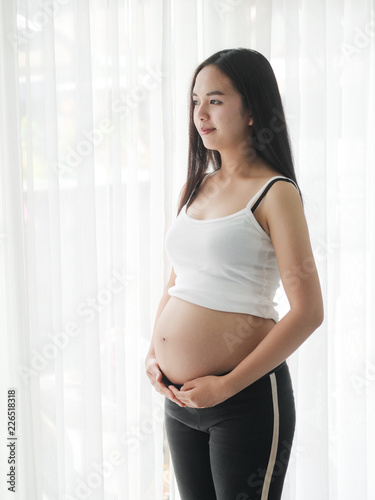 Asian pregnant woman touching her belly near window, lifestyle concept. Free Download Asian pregnant woman touching her belly near window, lifestyle concept. - GFXLoad