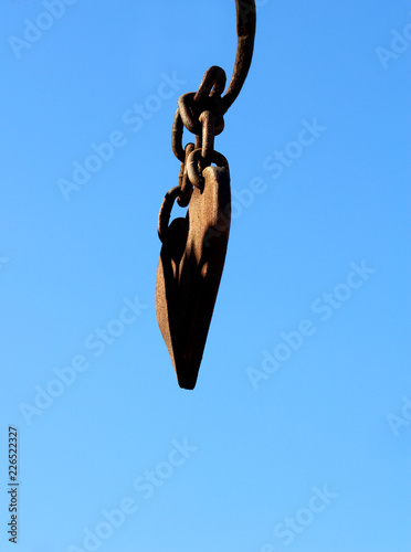 old metal heart with rings of chains suspended against a blue sky.