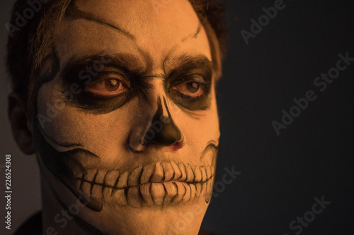 Portrait of a young man with a skull makeup for Halloween on a black background