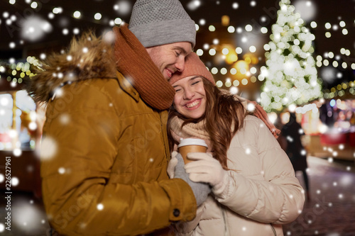 winter holidays, hot drinks and people concept - happy young couple with coffee at christmas market in evening