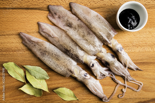 group of fresh squids next to a bowl with ink and some laurel leaves on a wooden board
 photo