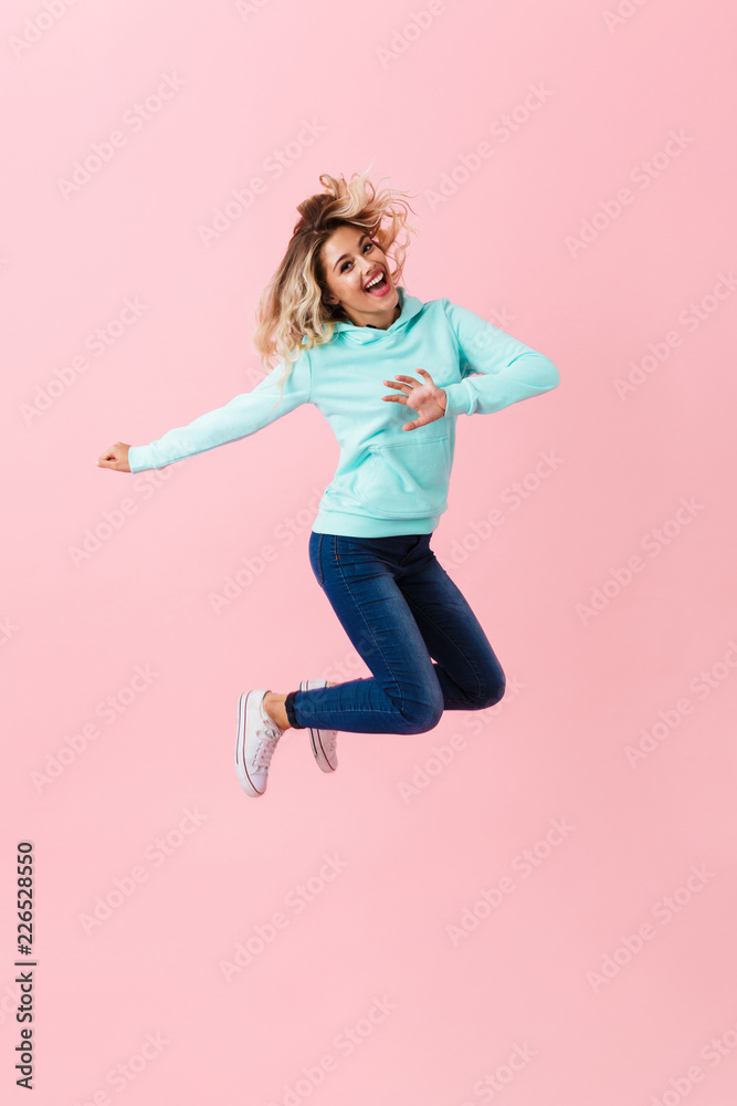 Full length image of cheerful woman in basic clothing jumping and laughing, isolated over pink background