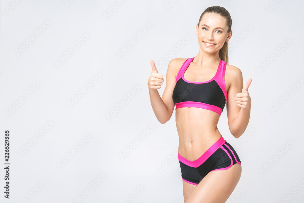 Smiling attractive sport woman showing thumb up sign isolated over gray background. Looking at camera. Smiling attractive sport woman showing thumb up sign isolated over gray background. Looking at camera.