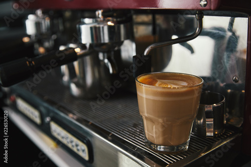 close-up view of glass cup with cappuccino and coffee maker