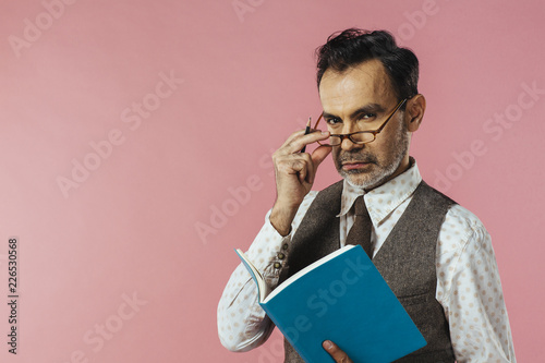 Portrait of  a mature man in vest holding notebook, glasses and notebook, isolated on pink