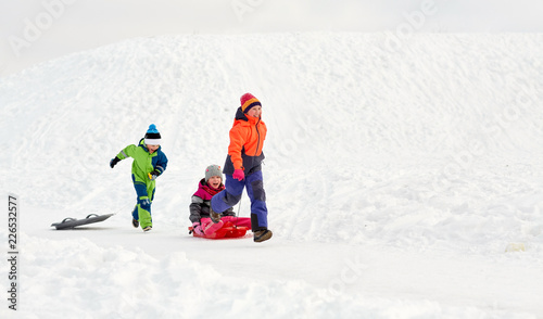 childhood, leisure and season concept - group of happy little kids in winter clothes with sled having fun outdoors