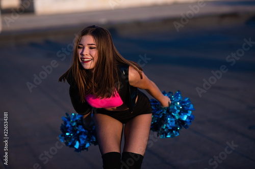 cheerleader with pompoms dancing outdoors on the roof at sunset