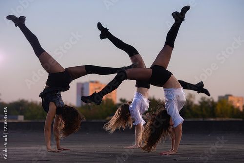 Girls cheerleaders with pompoms perform acrobatic element outdoors on the roof